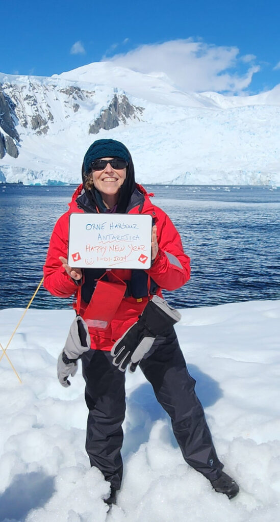 A woman in red jacket holding up sign on snow covered ground.